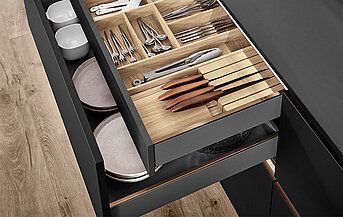 Offener nobilia nBOX Schubkasten in Schiefergrau mit Besteckeinsatz, Messern, Tellern und Schalen, modernes Design.